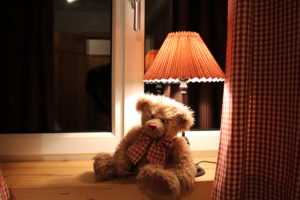 Der knufflige TeddyBär sitzt unter der Lampe im Fenster